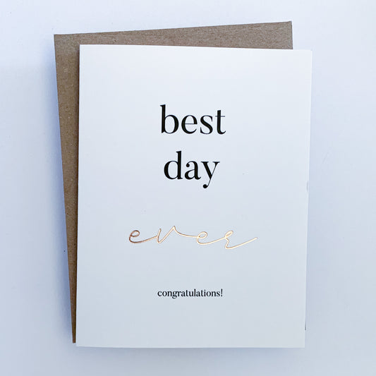 A Congratulation Card with a white background and black text that reads 'best day ever congratulations!' Where the word ever is written in gold foil.