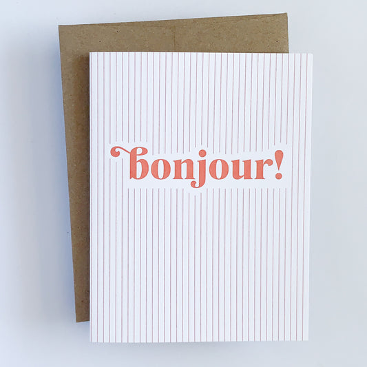 A greeting card with vintage-inspired red stripes and the word 'Bonjour!' printed in the center, accompanied by a kraft envelope.