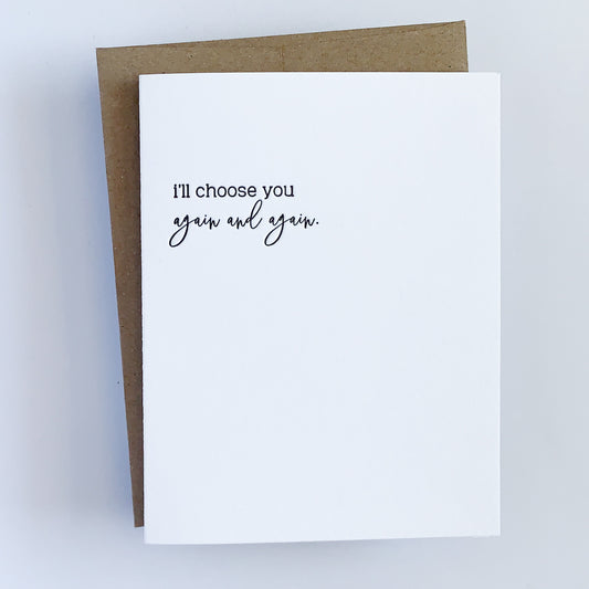A white letterpress greeting card with the text 'I'll choose you again and again' printed in black on the front, accompanied by a kraft envelope.