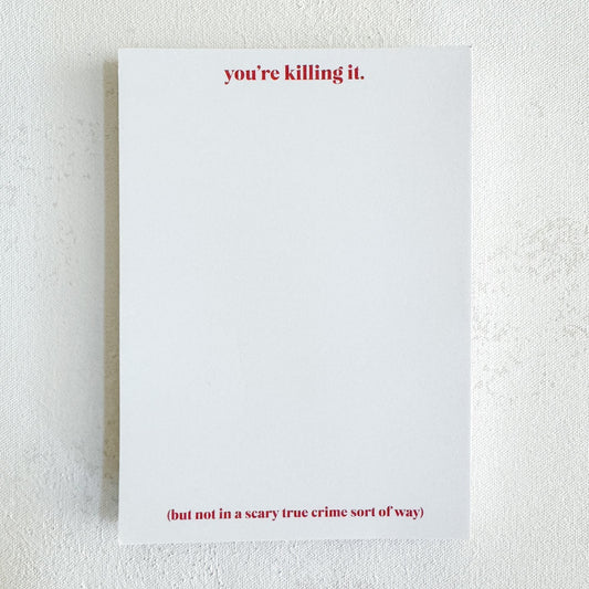 A Notepad with pink text at the top that reads 'You’re Killing It.' and pink text at the bottom that reads '(but not in a scary true crime sort of way)'.