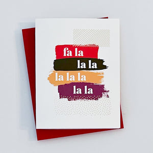 A holiday greeting cards with 'Fa la la la la la la la' text over colorful brushstrokes with gold foil details on a white background, paired with red envelopes.