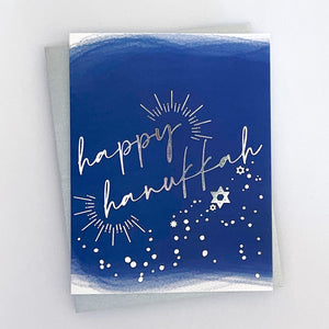 A blue card with 'Happy Hanukkah' text in silver foil, along with star and light designs.