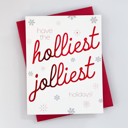 A holiday card with white background with snowflakes with red foil text that reads 'have the holliest jolliest holidays'