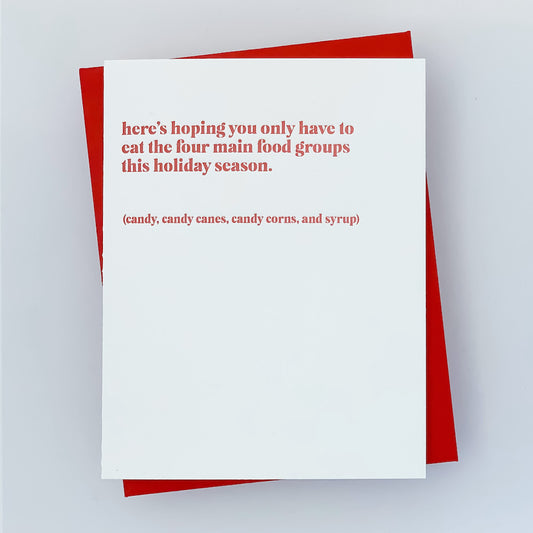 A holiday card with a blank interior, reads' here's hoping you only have to eat the four main food groups this holiday season' 'candy, candy canes, candy corns, and syrup' in red lettering. The card is presented with a red envelope.
