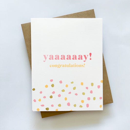 A congratulations card with ombre print and gold foil dots, featuring the text 'YAAAY! Congratulations' on the front, placed against a neutral background.