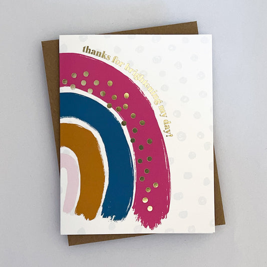A Thank You Card with a white background and light dots behind a brush stroke rainbow with gold foil dots and gold foil text that reads 'thanks for brighting my day!'