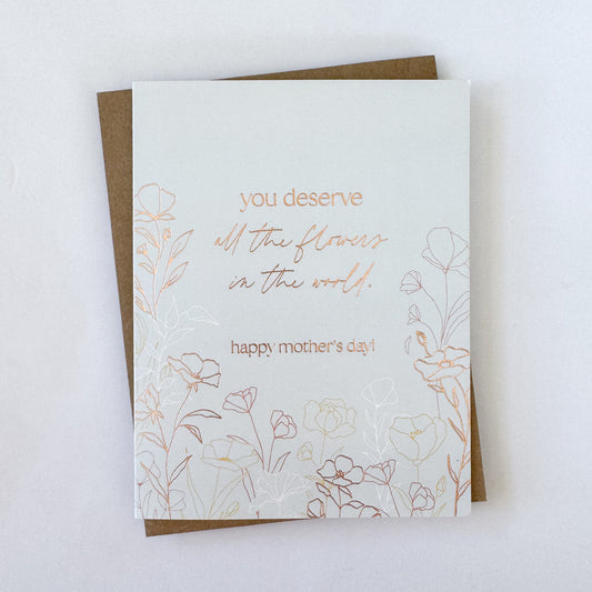 A Mother's Day card with a light blue background, copper foil text, and floral accents. The text reads 'you deserve all the flowers in the world.