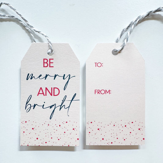 Gift Tag with silver and white string. The text reads 'Be Merry and Bright' written in pink and dark blue with pink and gold speckles on the bottom