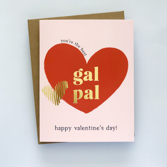 A valentines card with a pink background, featuring a red heart and the words 'you're the best' in a playful font, along with 'Gal Pal' and 'Happy Valentine's Day!' The card has gold foil accents and is shown with a kraft envelope.