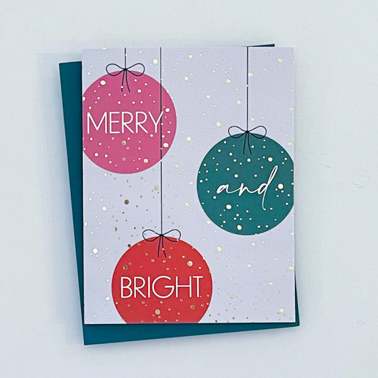A holiday card with three ornaments and gold foil accents. The text reads 'Merry and bright' 