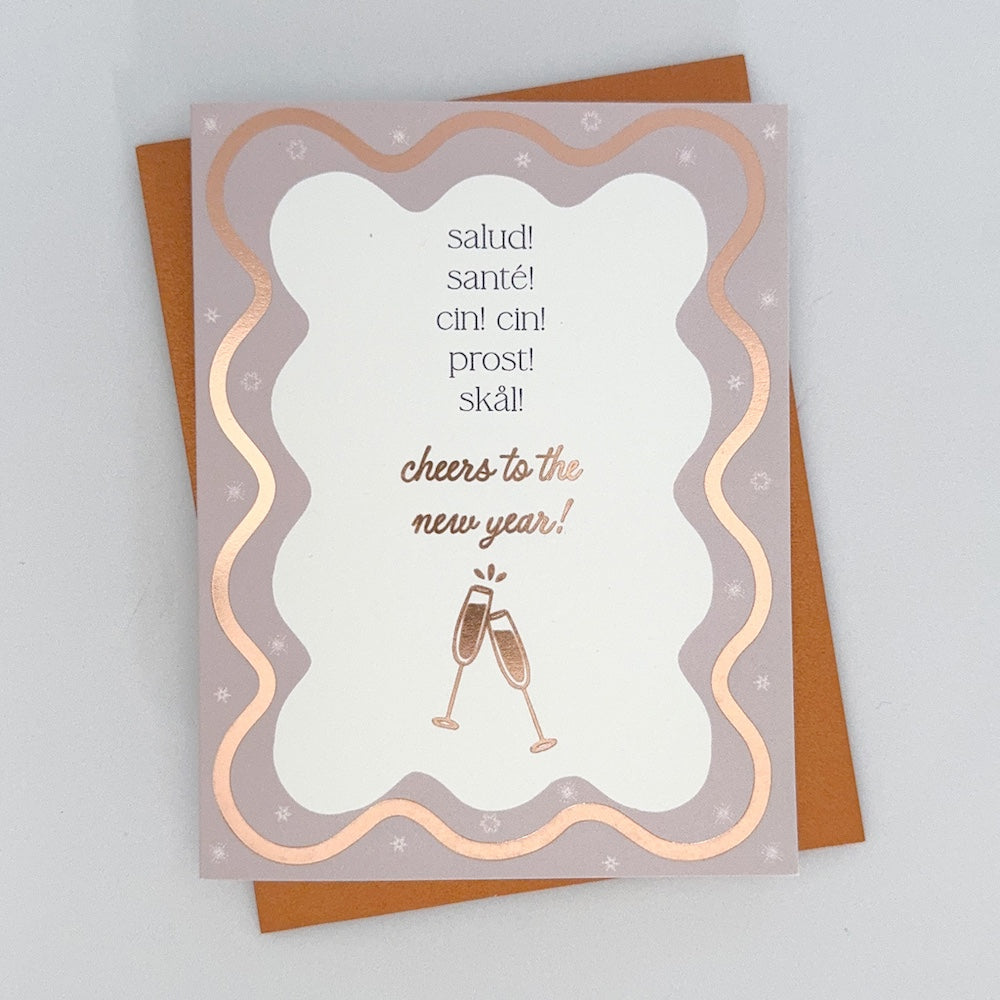 A Happy New Year Card with a wavy rose gold boarder featuring champaign flutes. The text reads 'Salud! Sante! Cin Cin! Prost! Skal! Cheers to the New Year!'.