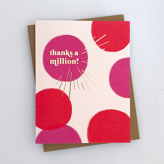A greeting card with a red and fuchsia dotted pattern and gold foil lettering that reads 'THANKS A MILLION!' The card also features a shiny gold foil starburst accent.