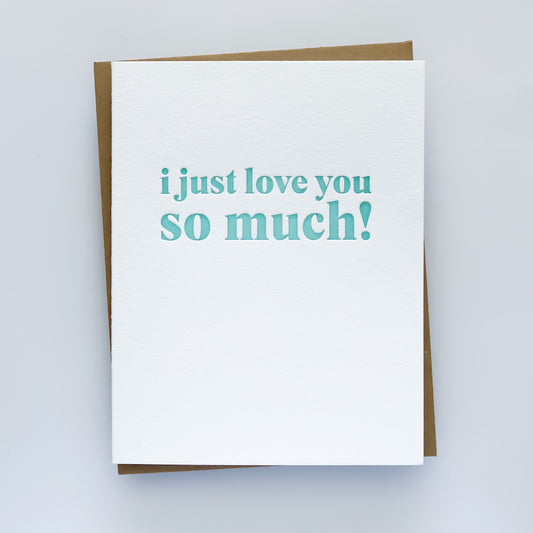 A white letterpress card with the phrase 'I JUST LOVE YOU SO MUCH!' printed in seafoam blue, accompanied by a kraft envelope.