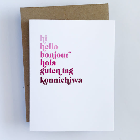 A multilingual greeting card with various texts in different colors. The text reads ' Hi Hello Bonjour Hola Guten Tag Konnichiwa' presented on a white background with a Kraft envelope.