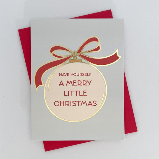 A holiday card that reads 'Have Yourself A Merry Little Christmas', featuring a red bow and a gold foil ornament design on a white background. The card is displayed with a red envelope behind it.