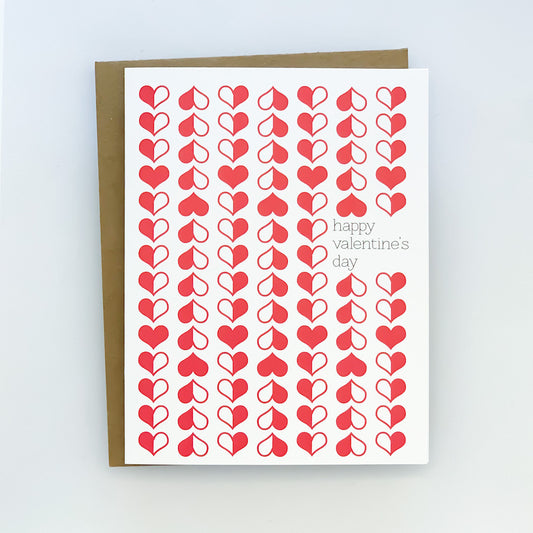 A Valentine's Day card with a retro-inspired design featuring rows of red heart shapes and the text 'Happy Valentine's Day' on a white background, paired with a kraft envelope.