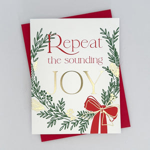 A Holiday Card with a green and gold foil wreath accents and a red ribbon. The text reads 'Repeat the Sounding Joy'