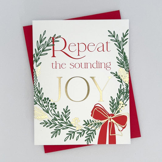 A Holiday Card with a green and gold foil wreath accents and a red ribbon. The text reads 'Repeat the Sounding Joy'