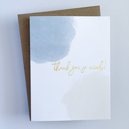A Greeting Card with a watercolor blue splotch and pink splotch framing the text 'Thank You So Much' written in gold foil.