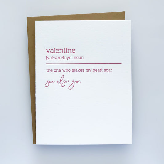 A letterpress card with pink text that reads 'Valentine [val-uhn-tayn] noun the one who makes my heart soar see also: you'. Written in definition format 