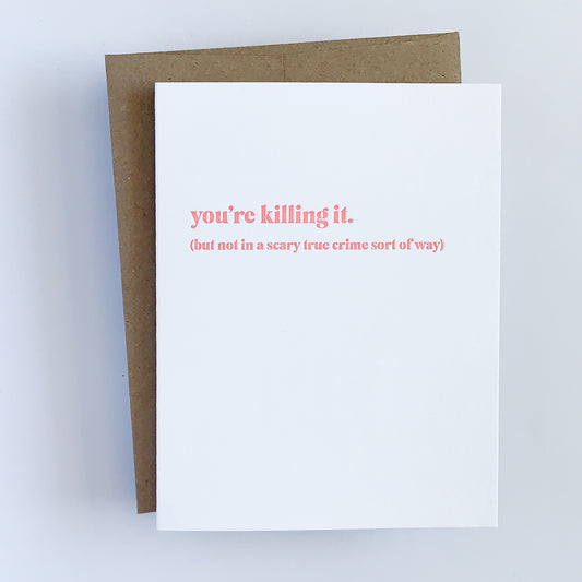 A greeting card with the phrase 'you're killing it. (but not in a scary true crime sort of way' printed in coral letterpress on the front, paired with a kraft envelope. 